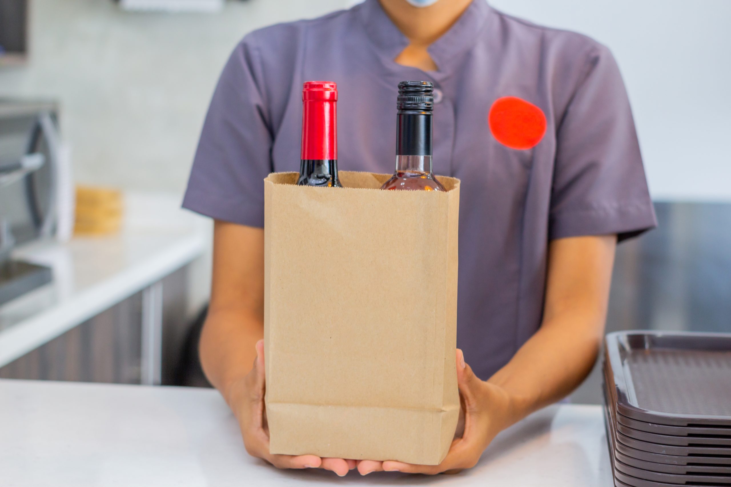 Young employee delivering customer’s purchase in to-go bag. livraison de vin à un restaurant